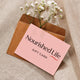Nourished Life Gift Card, a pink card on a kraft envelope with sprigs of white flowers above it, on a linen backdrop, clear product photo
