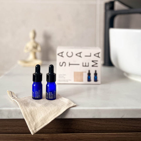 Two blue dropper bottles of blue lotus serum and face oil sitting on top of lotus silk cloth on a bathroom vanity.