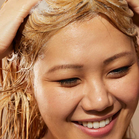 Woman with wet hair smiling while lathering ultra hydrating shampoo.