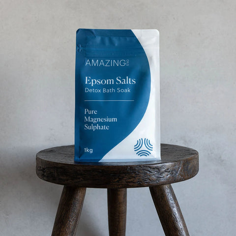 Amazing You Epsom Salts Detox Bath Soak 1kg lifestyle shot of the blue pouch on a dark wooden stool against a grey wall, styled lifestyle photo