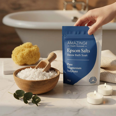 Amazing You Epsom Salts Detox Bath Soak lifestyle shot of a hand holding the blue pouch beside a bowl of salts, a sponge and candles
