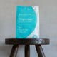 Amazing You Magnesium Daily Bath Flakes Pure Magnesium Chloride 800g lifestyle shot of the teal pouch on a dark wooden stool against a grey wall