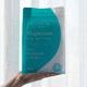 Amazing You Magnesium Daily Bath Flakes Pure Magnesium Chloride 800g lifestyle shot of a hand holding the teal pouch in front of a white curtain