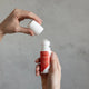 Amazing You Magnesium Joint Gel 60ml lifestyle shot of two hands lifting the cap off the roll-on bottle against a grey wall, styled lifestyle photo