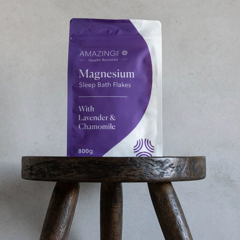 Amazing You Magnesium Sleep Bath Flakes 800g lifestyle shot of the purple pouch standing on a dark wooden stool against a grey wall