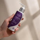 Amazing You Magnesium Sleep Lotion 125ml lifestyle shot of a hand holding the purple banded pump bottle against a beige wall, styled lifestyle photo