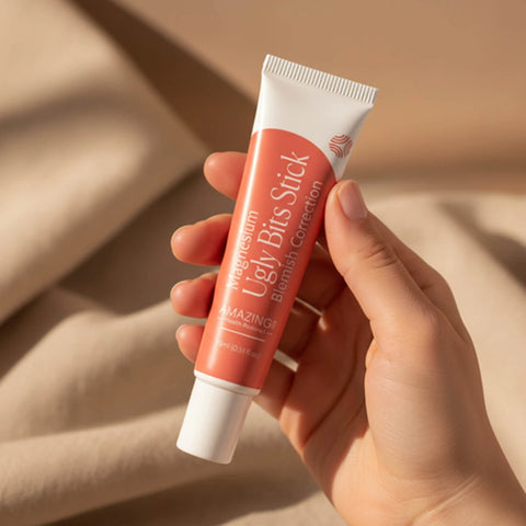 Amazing You Ugly Bits Stick 15ml lifestyle shot of a hand holding the coral red tube against a beige cloth, styled lifestyle photo