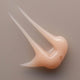 Close up of a swatch of peach coloured creamy hydrating gel on a beige background.