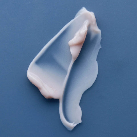 Swatch of pale purplish-pink night recovery cream on a blue background.