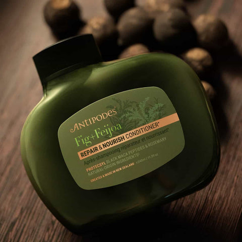 Green bottle of Antipodes Fig + Feijoa Conditioner on a wooden surface.