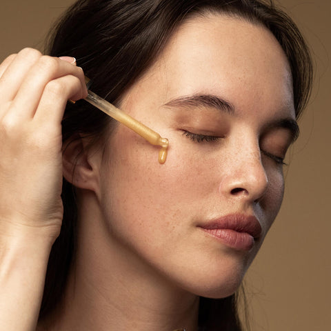 Model applying glow vitamin c serum to her cheek with dropper applicator.