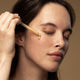 Model applying glow vitamin c serum to her cheek with dropper applicator.