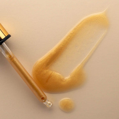 Dropper applicator with golden vitamin c brightening serum with a swatch on a pale background.