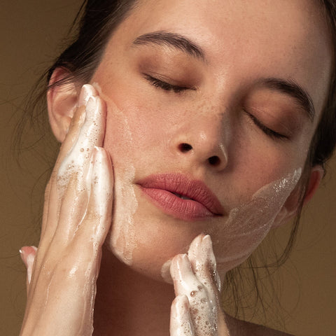 Model massaging foamy glow gel cleanser into her cheeks.