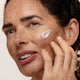 Woman applying jasmine flower cream to her face with a neutral background