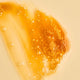 Swatch of Juliet Anti-Blemish Gel Cleanser with caramel colouring and light texture with bubbles on a pale yellow background.