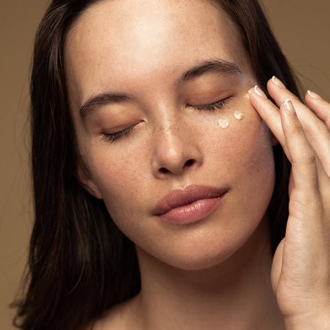 Antipodes Kiwi Seed Gold Luminous Eye Cream lifestyle close up of a woman with closed eyes and dabs of cream under her eyes, styled lifestyle photo