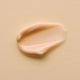 Swatch of smooth & creamy kiwi seed gold luminous eye cream on a pale peach background.