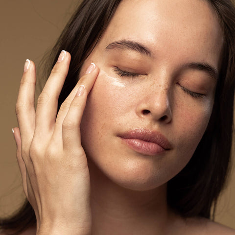 Model applying kiwi seed oil eye cream to her under eye area.