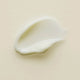 Swatch of Kiwi Seed Oil Eye Cream with smooth and creamy texture and a pale white shade on a cream background.