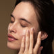 Model applying lime caviar collagen rich firming cream to her cheek.