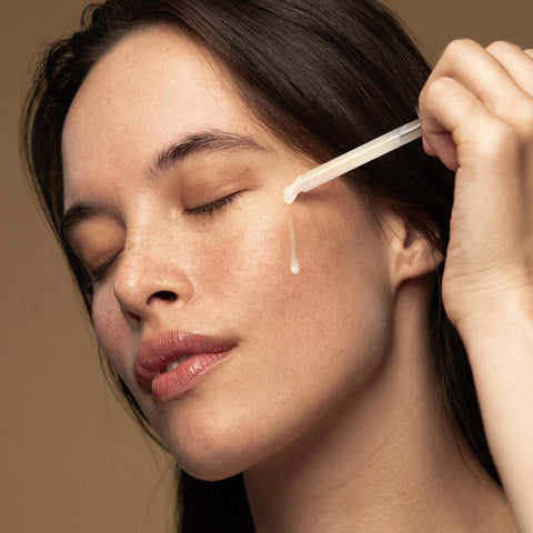Model applying maya serum to her cheek with dropper applicator.
