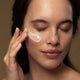 Model applying hydrating day cream to her cheek.