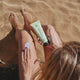Person applying sunscreen to their leg on a sandy beach.