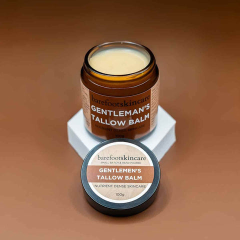 Jar of Gentleman's Tallow Balm with lid on a brown background, showing texture of balm.