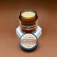 Jar of Gentleman's Tallow Balm with lid on a brown background, showing texture of balm.