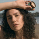 Black Chicken Remedies Axilla Deodorant Paste Barrier Booster lifestyle shot of a woman with curly hair holding the closed tin against her forehead