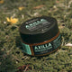 Black Chicken Remedies Axilla Deodorant Paste Original 75g tin sitting on green grass and moss, outdoor lifestyle shot of the closed tin
