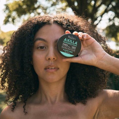 Black Chicken Remedies Axilla Deodorant Paste Original Plastic Free 60g lifestyle shot of a woman with curly hair holding the closed tin over one eye