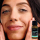 Black Chicken Remedies Complexion Polish lifestyle close up of a woman touching her cheeks while holding the small bottle near her face