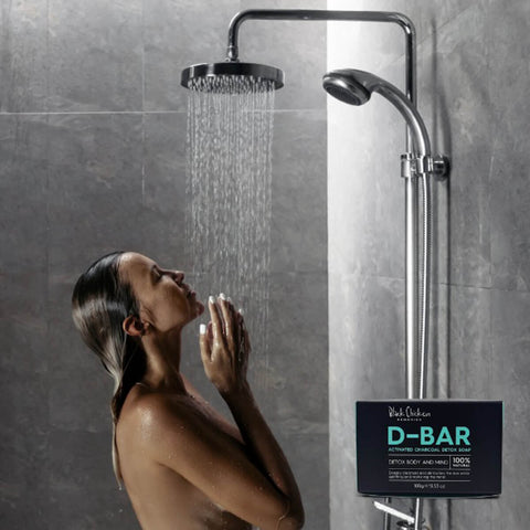 Black Chicken Remedies D-Bar Activated Charcoal Detox Soap 100g lifestyle shot of a person showering, with the black box in the corner