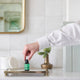 Black Chicken Remedies Essential Oil Blend De-Stress 9ml lifestyle shot of a hand placing the small bottle on a brass tray beside a bud vase
