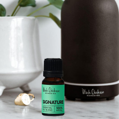 Black Chicken Remedies Essential Oil Blend Signature lifestyle shot of the small bottle in front of a dark diffuser and a white vase