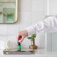 Black Chicken Remedies Essential Oil Blend Signature lifestyle shot of a hand placing the small bottle on a brass tray beside a bud vase and mirror