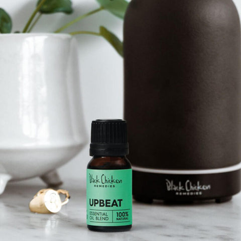 Black Chicken Remedies Essential Oil Blend Upbeat lifestyle shot of the small bottle in front of a dark diffuser and a white vase