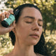Black Chicken Remedies HairOM Hair & Scalp Oil 50ml lifestyle shot of a woman with wet dark hair applying the oil to her scalp, trees behind her
