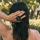 Black Chicken Remedies HairOM Hair & Scalp Oil 50ml lifestyle shot of a person with wet hair seen from behind, one hand on their hair