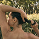 Black Chicken Remedies HairOM Hair & Scalp Oil 50ml lifestyle shot of a person from behind, running a hand through wet hair outdoors