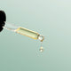 Black Chicken Remedies Love Your Face Serum lifestyle shot of a glass dropper over a pale green backdrop with a drop of serum falling