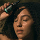 Black Chicken Remedies Love Your Face Serum lifestyle shot of a woman with curly hair and closed eyes holding the dropper bottle near her forehead
