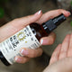 Hand holding a bottle of 'Face Magic' organic castor oil face oil with a spray nozzle.