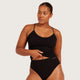 Boody Base Layer Cami Top Black lifestyle shot of a woman wearing the black cami and black briefs with a hand at the hem, styled lifestyle photo