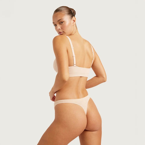 Boody G-String Shell lifestyle back view of a woman looking over her shoulder in a nude bra and nude g-string, styled lifestyle photo