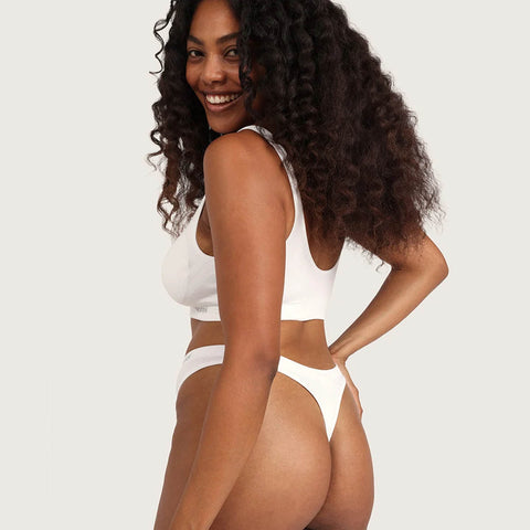 Boody G-String White lifestyle back view of a smiling woman with curly hair in a white bra and the white g-string, styled lifestyle photo