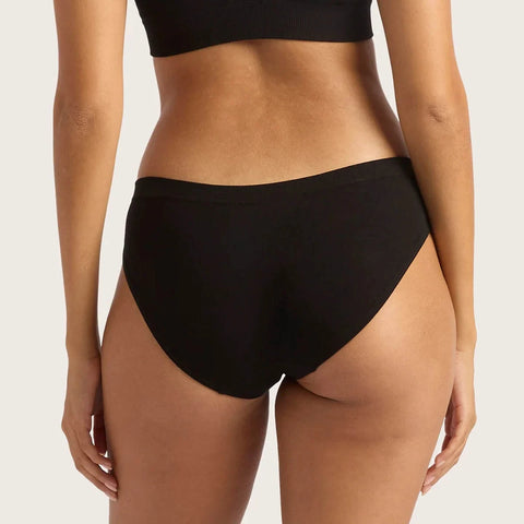 Boody Hipster Bikini Black lifestyle back view of a person wearing the black bikini briefs and a black crop top, plain backdrop