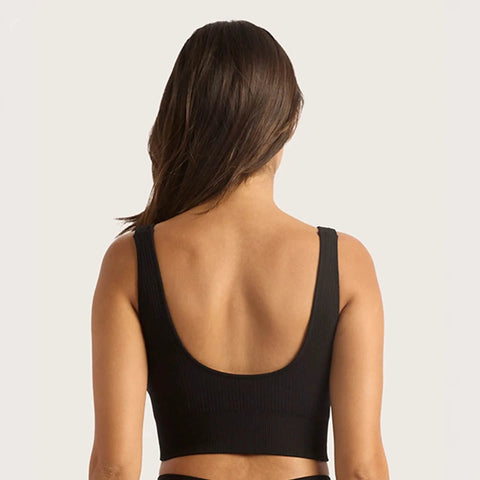 A woman viewed from the back wearing a black ribbed scoop-neck sports bra or crop top against a plain light background.